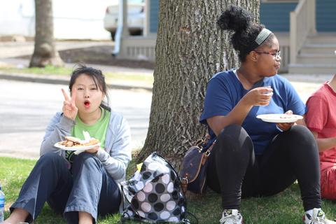 Photo of girls under tree eating pizza and flashing peace sign.