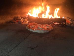 Photo of interior of the oven with log fire and pizza baking.